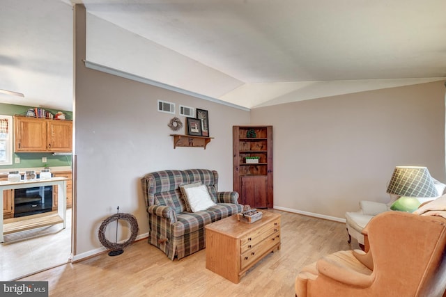 living area with beverage cooler, vaulted ceiling, and light hardwood / wood-style floors