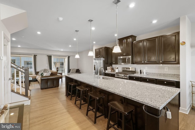 kitchen with appliances with stainless steel finishes, a sink, dark brown cabinetry, light wood-type flooring, and a kitchen breakfast bar