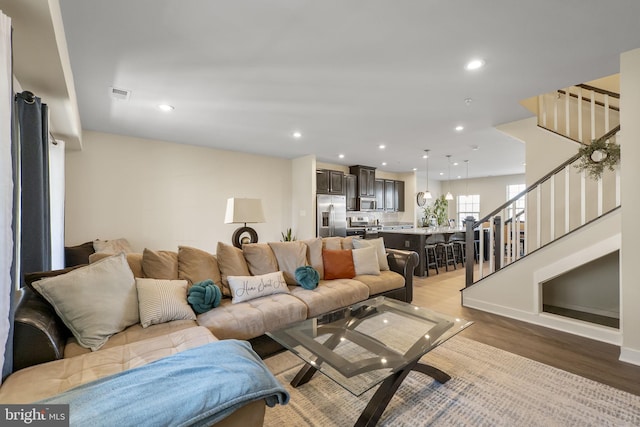 living room featuring visible vents, baseboards, light wood-style flooring, stairway, and recessed lighting