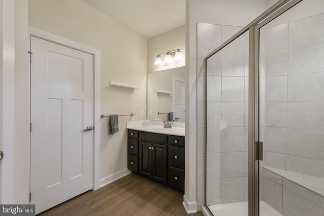 full bath featuring a stall shower, vanity, baseboards, and wood finished floors