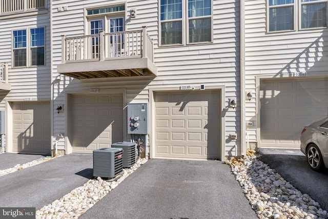 view of exterior entry with driveway, a balcony, an attached garage, and central AC unit