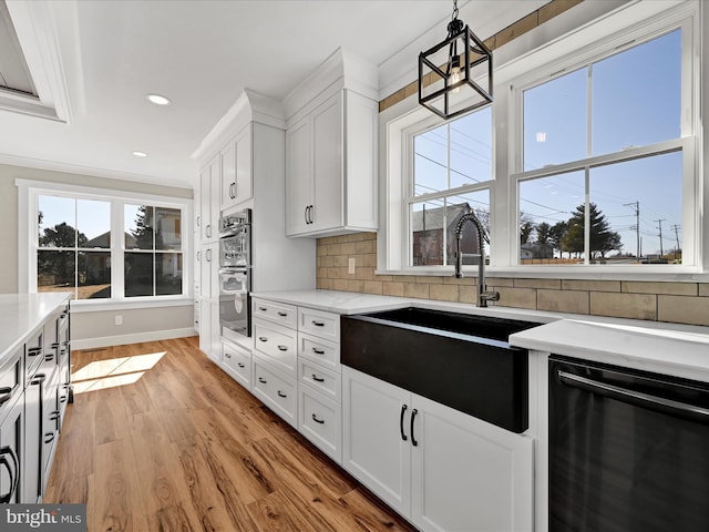 kitchen featuring light wood-type flooring, white cabinets, decorative light fixtures, sink, and black dishwasher