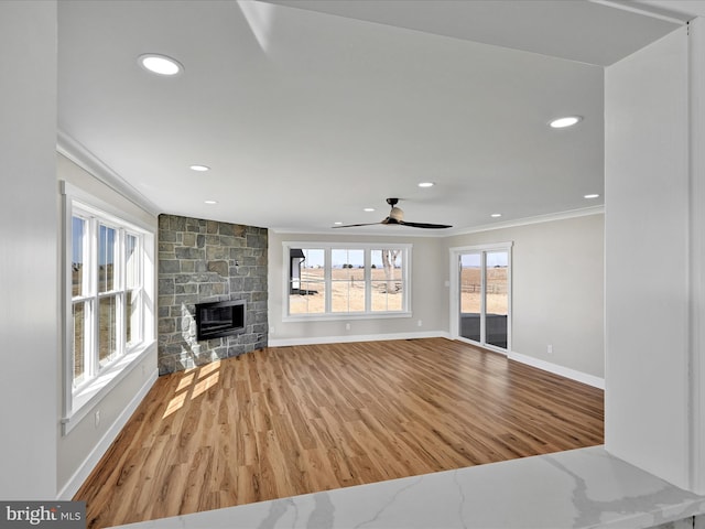 unfurnished living room featuring ceiling fan, ornamental molding, a stone fireplace, and hardwood / wood-style floors