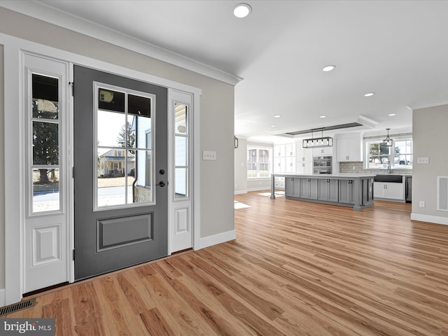 foyer entrance featuring light wood-type flooring, crown molding, and sink