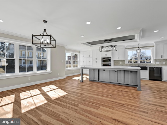 kitchen featuring a tray ceiling, a kitchen island, dishwasher, and pendant lighting