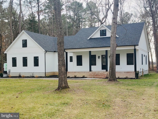 modern farmhouse featuring covered porch, a shingled roof, and a front yard