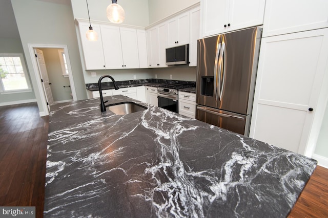 kitchen with decorative light fixtures, stainless steel appliances, white cabinetry, a sink, and dark stone countertops