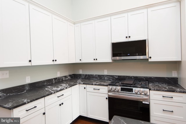 kitchen with stainless steel appliances, white cabinetry, and dark stone countertops