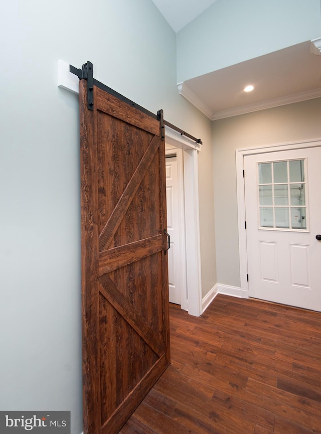 corridor featuring ornamental molding, a barn door, dark wood finished floors, and baseboards