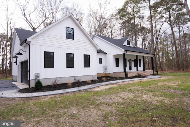 view of side of property featuring a garage, a lawn, roof with shingles, crawl space, and covered porch