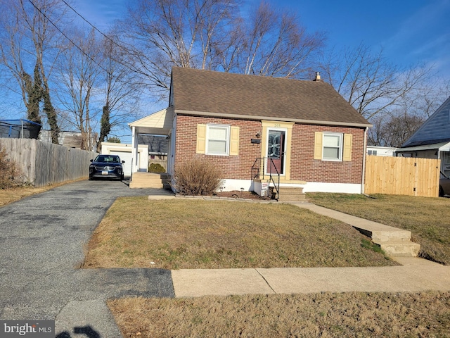 view of front of property featuring a front yard, brick siding, fence, and roof with shingles