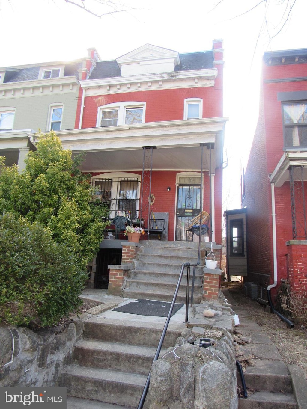 view of property featuring covered porch, brick siding, and mansard roof