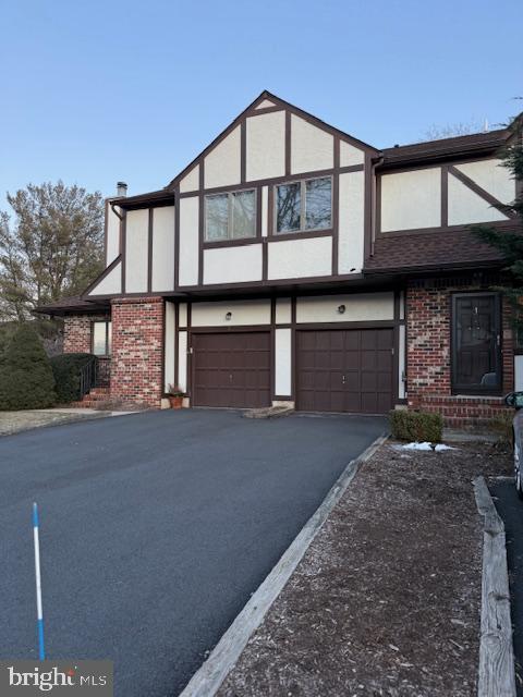 tudor home featuring a garage, driveway, brick siding, and stucco siding