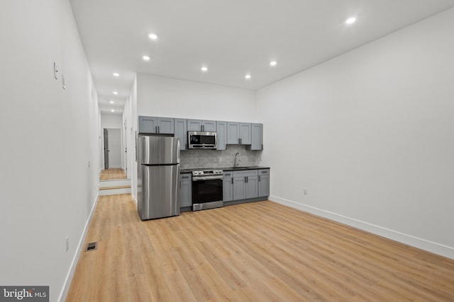 kitchen with gray cabinetry, stainless steel appliances, light hardwood / wood-style floors, sink, and tasteful backsplash