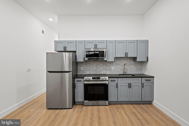 kitchen with sink, gray cabinetry, light hardwood / wood-style floors, stainless steel appliances, and tasteful backsplash