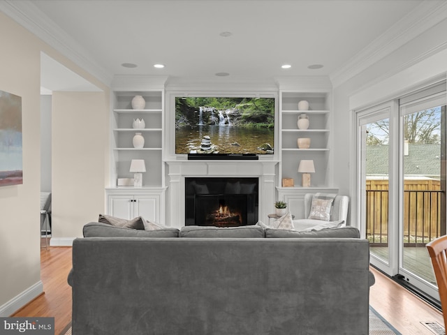 living area featuring built in features, baseboards, a lit fireplace, ornamental molding, and light wood-type flooring