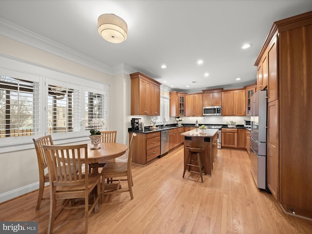 kitchen with light wood-style floors, ornamental molding, appliances with stainless steel finishes, a center island, and brown cabinetry