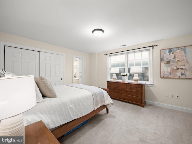 bedroom with a closet, visible vents, ensuite bathroom, light carpet, and baseboards