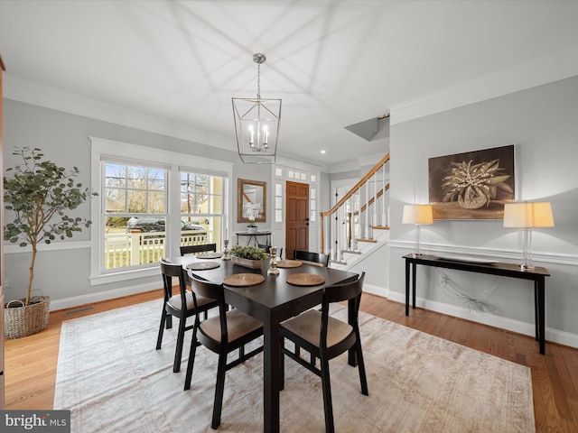 dining room with a notable chandelier, wood finished floors, visible vents, stairway, and crown molding