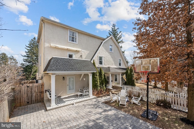 back of property with a shingled roof, a fenced front yard, a gambrel roof, and stucco siding