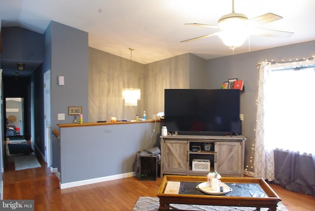 living area featuring a chandelier, wood finished floors, ceiling fan, lofted ceiling, and baseboards