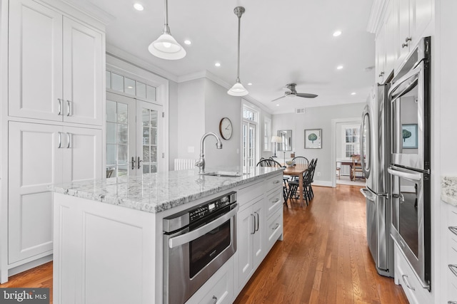 kitchen with an island with sink, french doors, white cabinets, decorative light fixtures, and sink