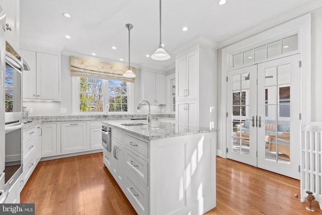 kitchen with an island with sink, white cabinets, and hanging light fixtures