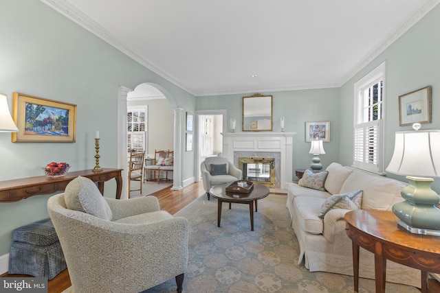 living room featuring a fireplace, ornamental molding, ornate columns, and light wood-type flooring