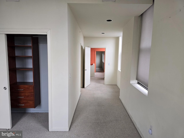 hall featuring baseboards and light colored carpet