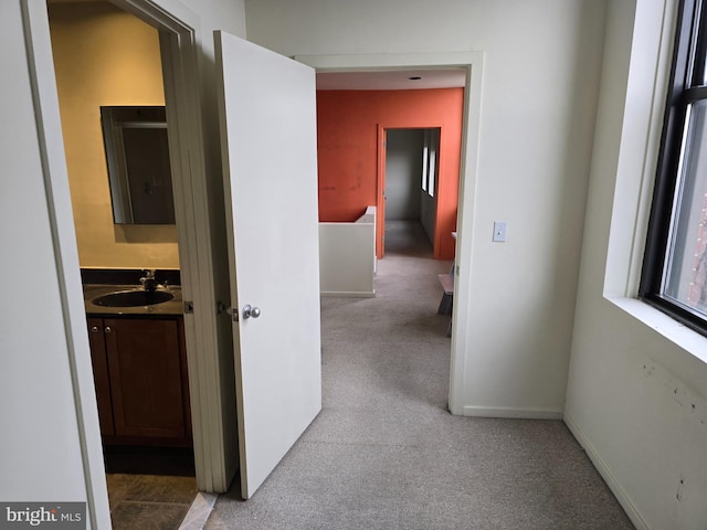 hallway featuring carpet, a sink, and baseboards