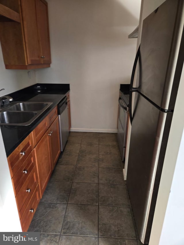 kitchen with appliances with stainless steel finishes, dark countertops, brown cabinets, and a sink