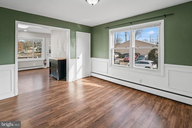 empty room with plenty of natural light, wood-type flooring, and a baseboard heating unit