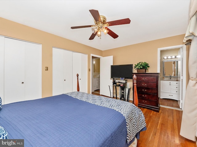 bedroom featuring connected bathroom, a ceiling fan, two closets, light wood-style floors, and a sink