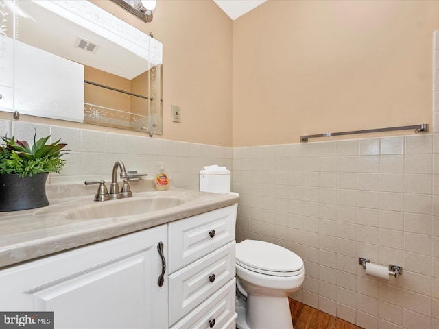 full bathroom with toilet, vanity, visible vents, tile walls, and wainscoting