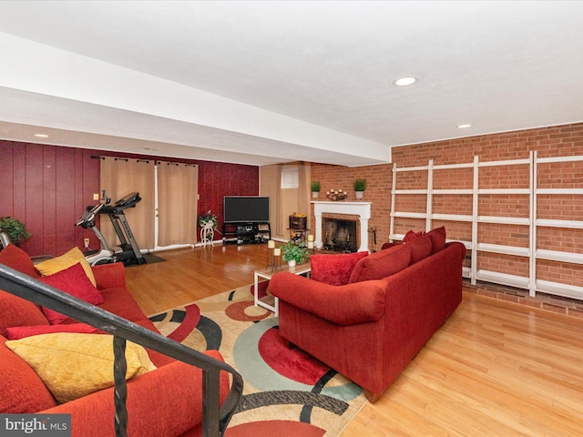 living room with recessed lighting, a brick fireplace, brick wall, and wood finished floors