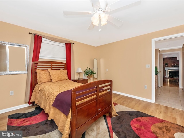 bedroom with baseboards, arched walkways, a ceiling fan, light wood-type flooring, and a fireplace