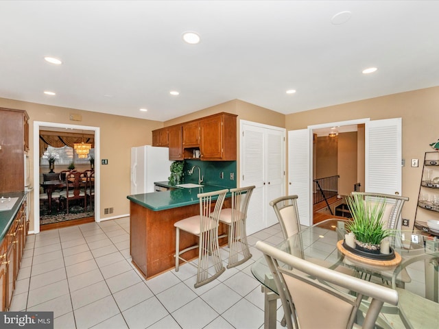 kitchen featuring light tile patterned floors, brown cabinetry, dark countertops, white fridge with ice dispenser, and a sink