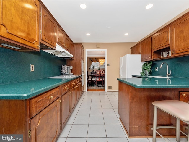 kitchen with white refrigerator with ice dispenser, brown cabinets, under cabinet range hood, and light tile patterned flooring