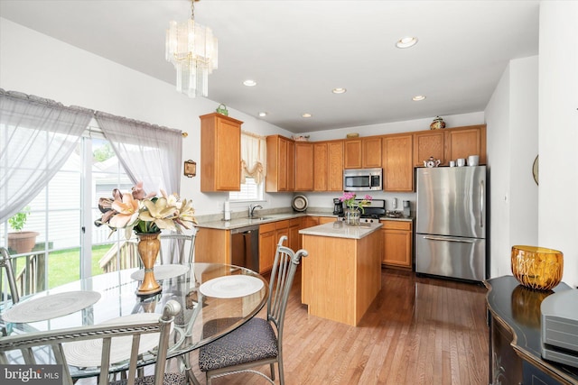 kitchen with light hardwood / wood-style flooring, hanging light fixtures, stainless steel appliances, a kitchen island, and sink