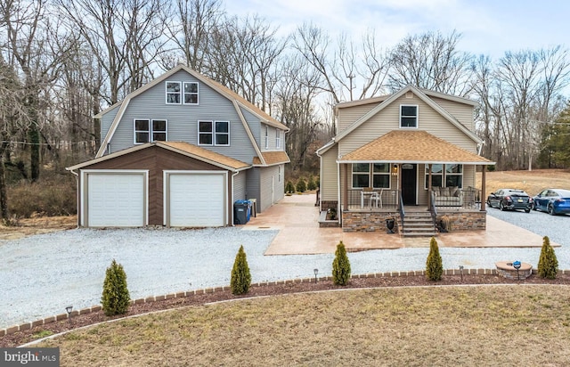 view of front of property with a porch, a garage, a gambrel roof, roof with shingles, and gravel driveway