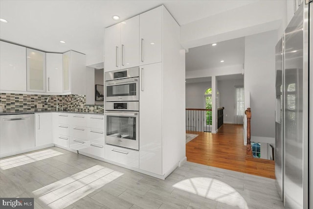 kitchen featuring light hardwood / wood-style flooring, sink, appliances with stainless steel finishes, white cabinets, and decorative backsplash