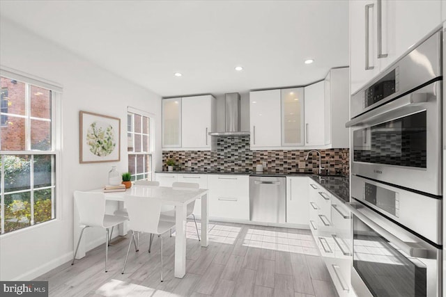 kitchen with appliances with stainless steel finishes, tasteful backsplash, wall chimney range hood, sink, and white cabinetry