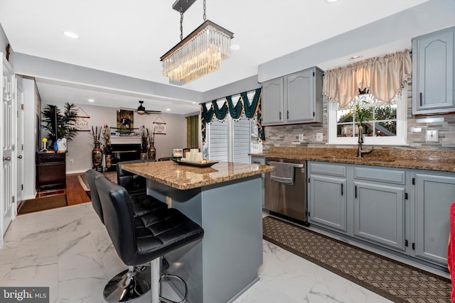 kitchen featuring a kitchen island, a kitchen breakfast bar, marble finish floor, dishwasher, and pendant lighting