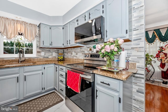 kitchen with stainless steel appliances, dark stone counters, a sink, and tasteful backsplash