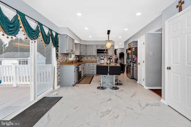 kitchen featuring pendant lighting, stainless steel appliances, tasteful backsplash, gray cabinets, and a kitchen bar