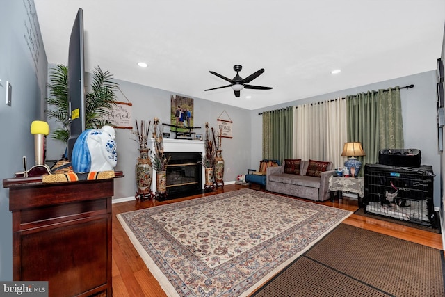 living room with a fireplace with flush hearth, ceiling fan, baseboards, and wood finished floors