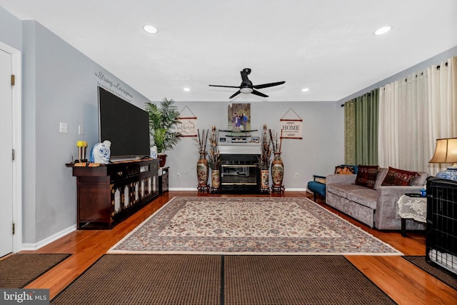 living area with a glass covered fireplace, ceiling fan, recessed lighting, and wood finished floors