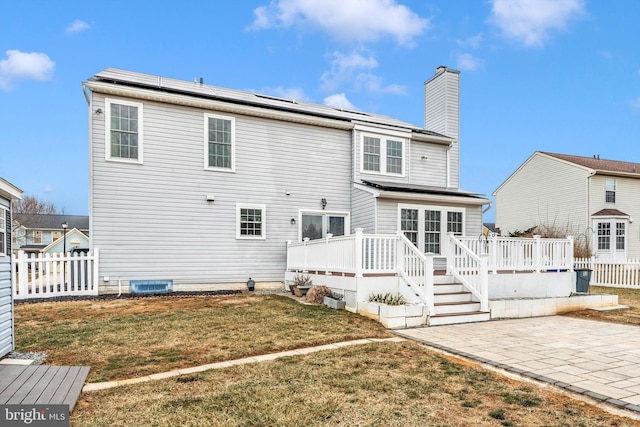 back of property featuring a patio area, a lawn, a deck, and solar panels