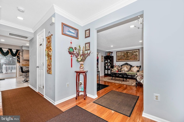 hall with baseboards, light wood-style flooring, visible vents, and crown molding