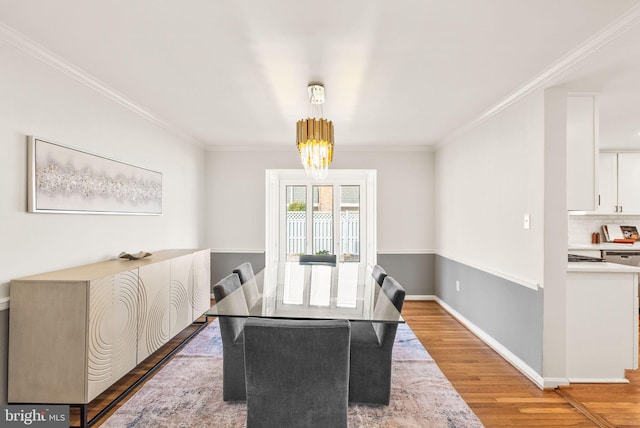 dining space with light wood-style flooring, crown molding, baseboards, and a notable chandelier